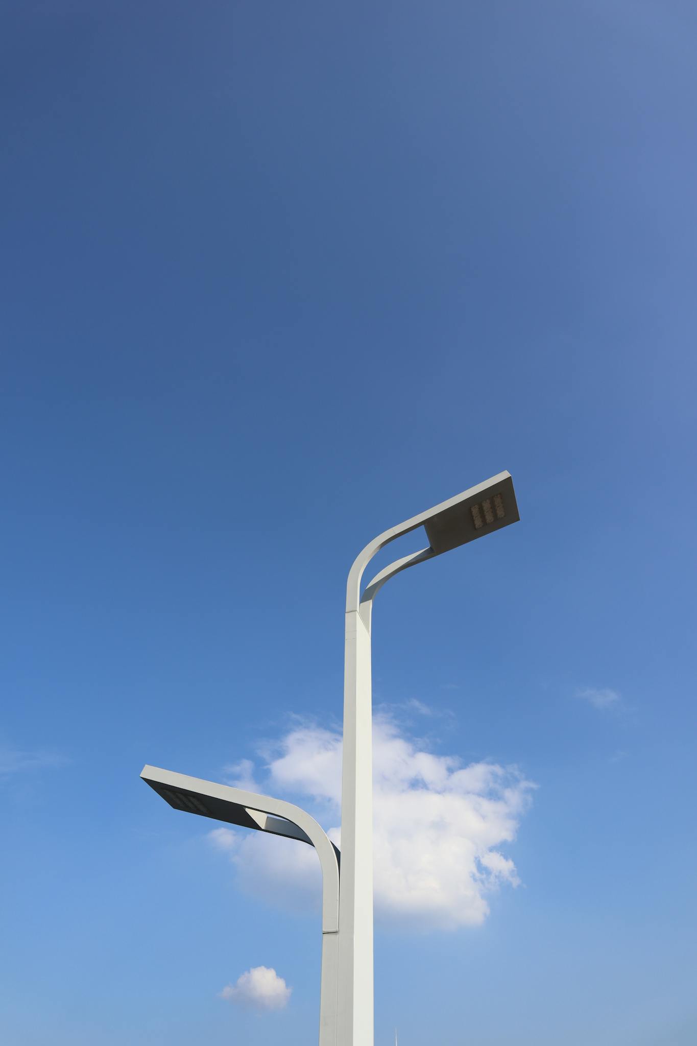 A minimalist view of contemporary streetlights under a bright blue sky with a few clouds.