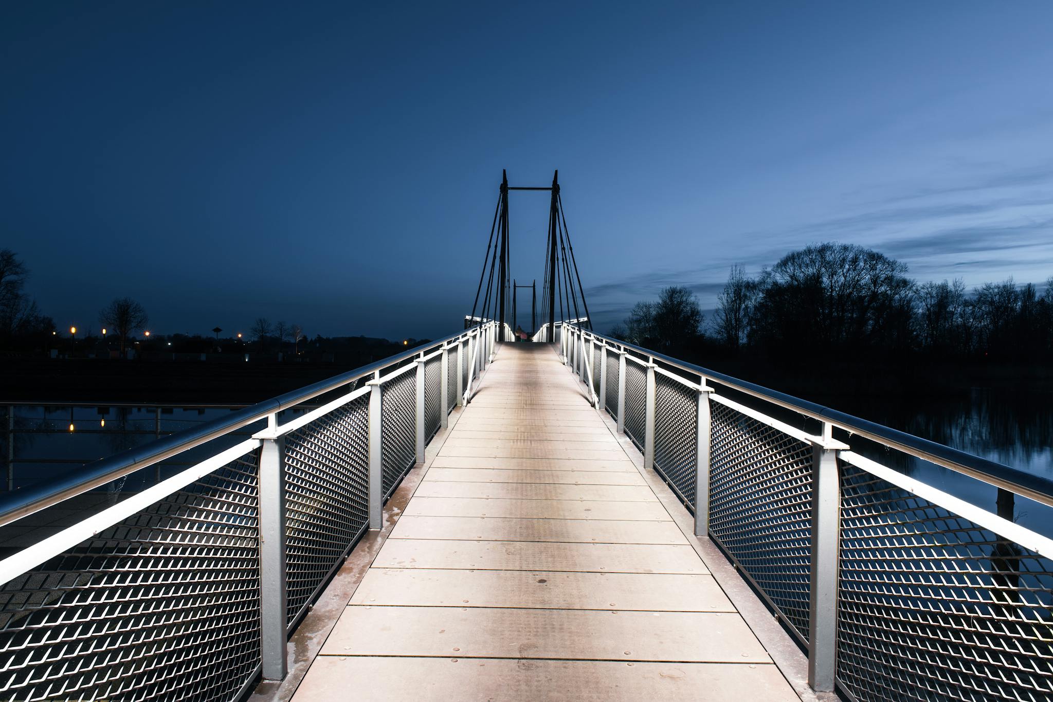 An illuminated suspension footbridge in Geesthacht during the tranquil blue hour, showcasing modern architecture.