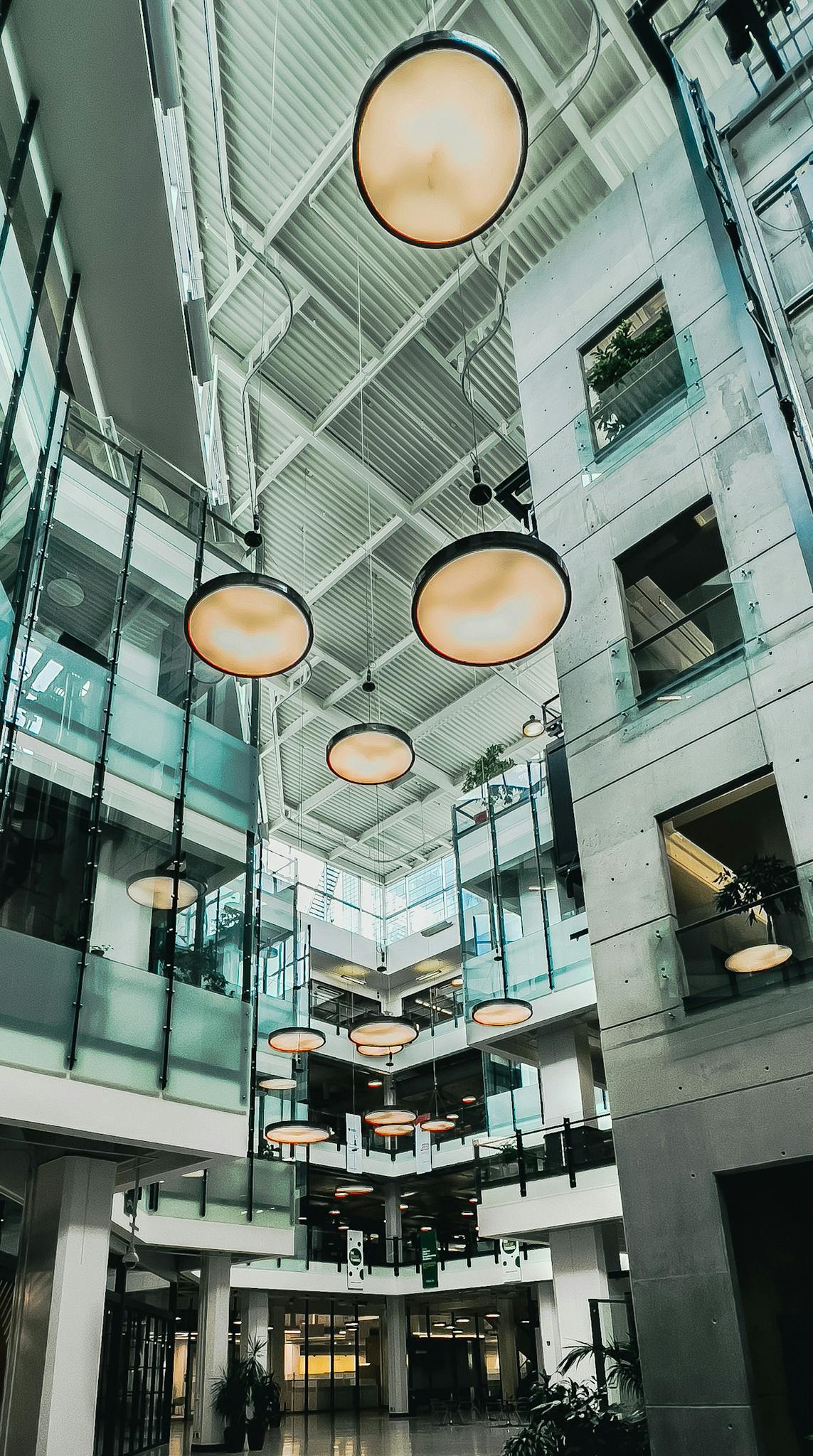 Interior of a modern office building with glass railings and pendant lights, shot from a low angle.
