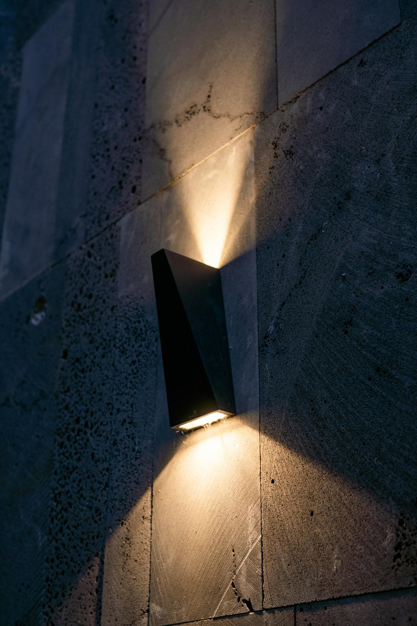Stylish modern wall sconce light emitting warm light against a textured concrete wall.